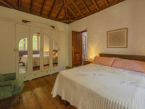 Una camera da letto con un letto grande, un armadio con ante a specchio, una poltrona verde e un soffitto in legno.