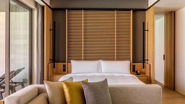 Une chambre d’hôtel moderne avec un lit, un canapé, une table basse avec des fruits et une grande fenêtre.