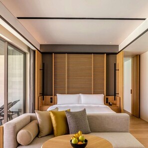 Una habitación de hotel moderna con una cama, un sofá, una mesa de centro con fruta y un ventanal grande.