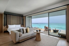 Un dormitorio moderno con una cama grande, un sofá, una mesita redonda y un balcón con vistas al océano.