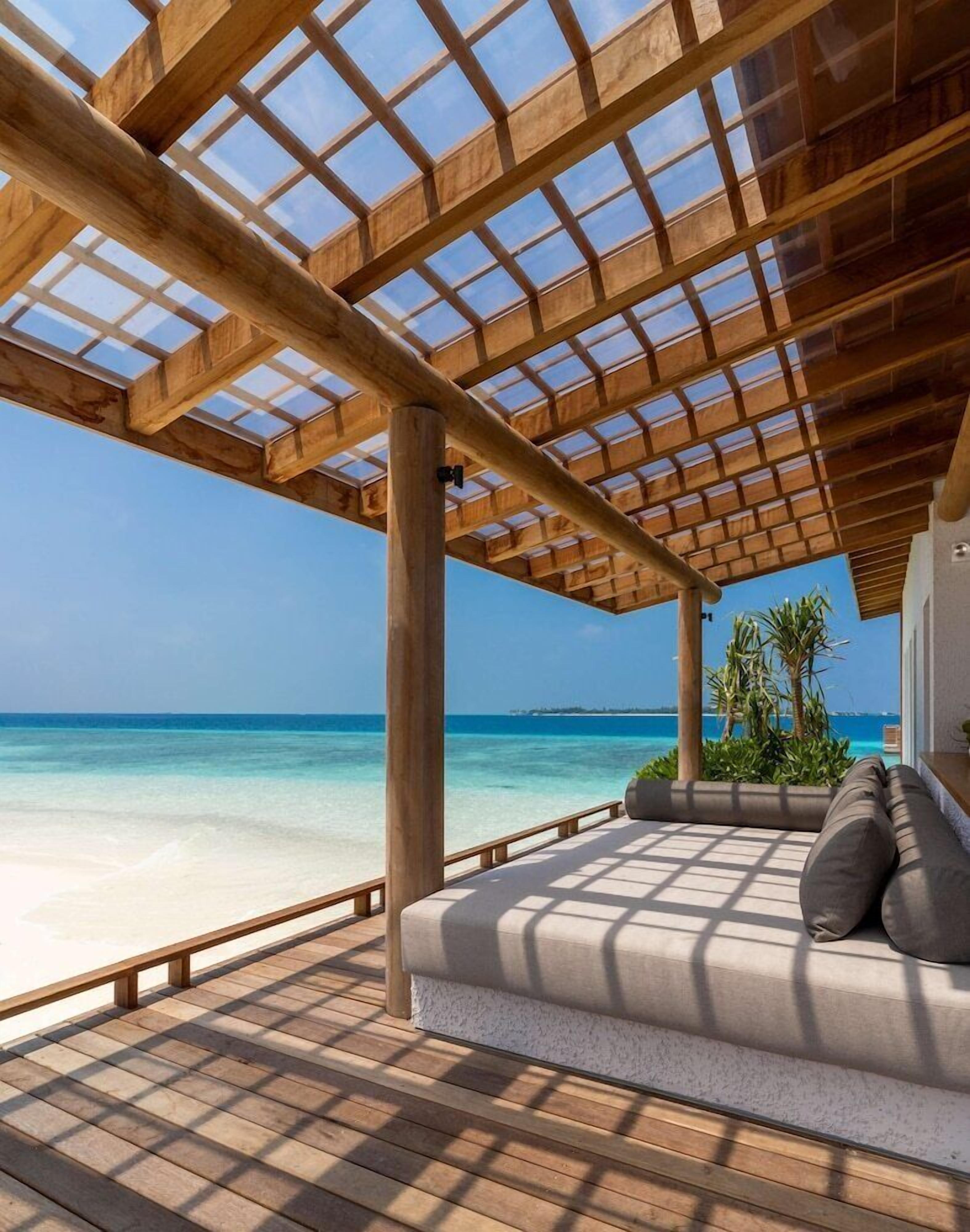 Terraza de madera con techo de vidrio que da a una playa.