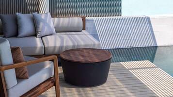 A deck with a sofa and a round table, overlooking a pool.