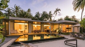 Une maison moderne dotée d’une piscine, de chaises longues et d’un jardin tropical.