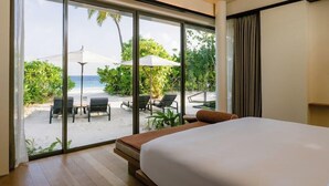 Une chambre d’hôtel dotée d’une grande porte-fenêtre coulissante donnant sur la plage, d’un lit et d’une petite table.