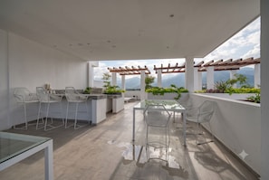 An outdoor patio with a glass table and chairs, a barbecue area, and a view of mountains. - Luxury 1BR Condo Grand Trianon Puerto Vallarta (Puerto Vallarta)