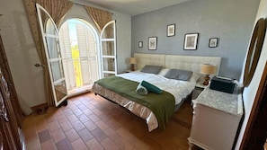 A bedroom with a bed, a nightstand, a dresser, and a window with curtains.