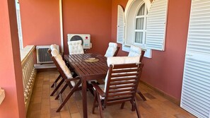 A patio with a wooden table and chairs, an air conditioning unit, and a window with shutters.
