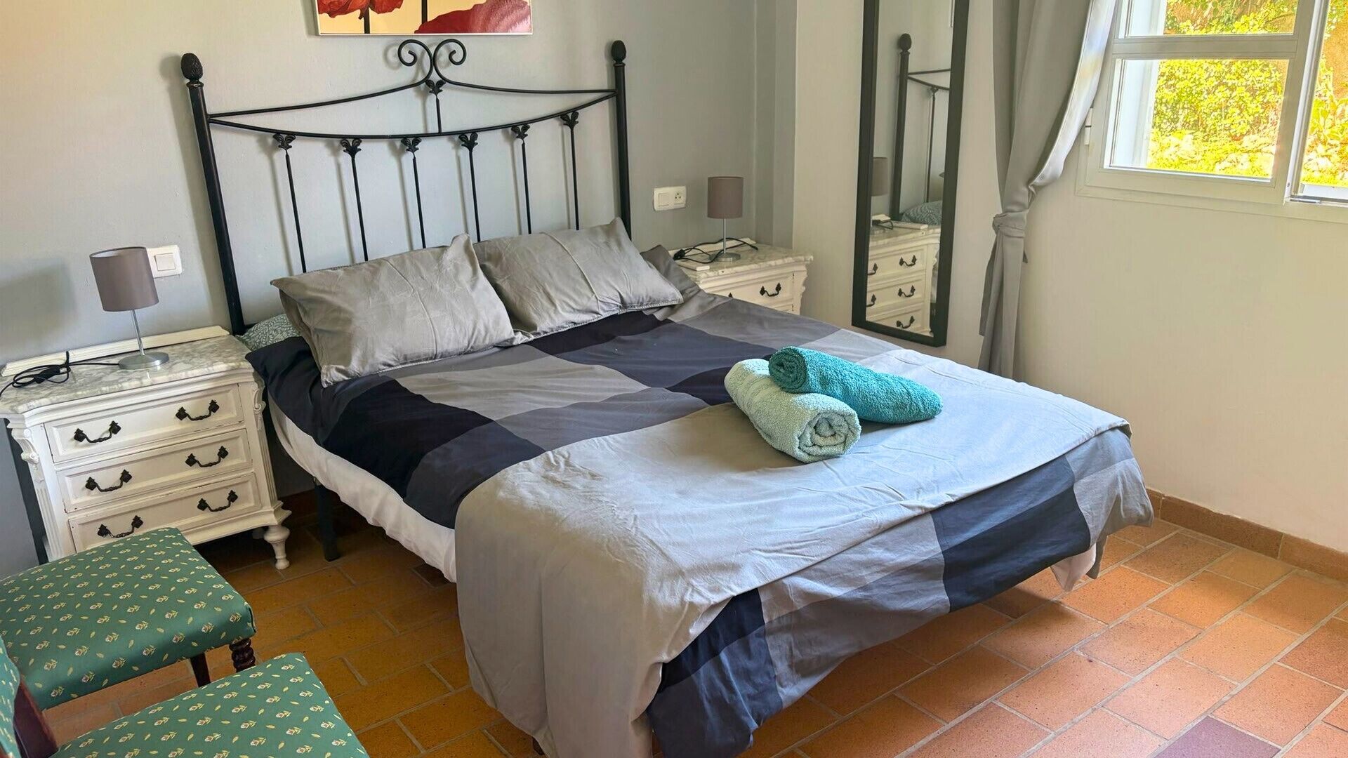 Une chambre à coucher comprenant un lit, des tables de chevet, un banc, un miroir et une fenêtre.