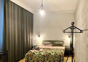 A bedroom with a bed, a hanging light fixture, a bedside table, and a wall-mounted light.