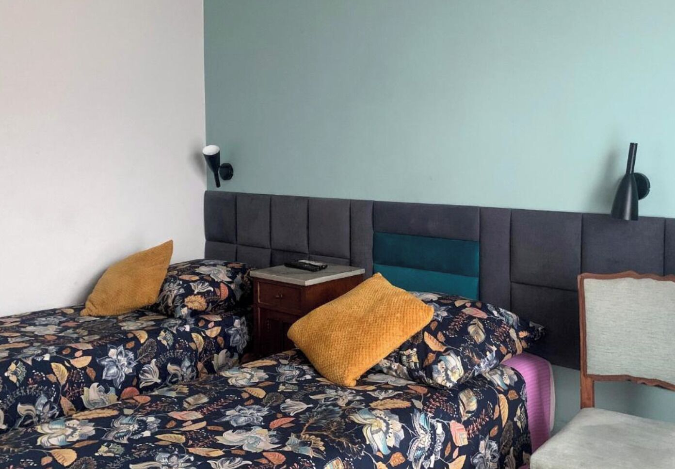 A hotel room with two beds, a nightstand, a lamp, and a chair.