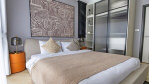 A modern bedroom with a large bed, a side table, a wall-mounted artwork, and a wardrobe. - The Title Legendary Designer 2BR near Bang Tao Beach (Tambon Choeng Thale)