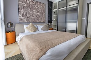 A modern bedroom with a large bed, a side table, a wall-mounted artwork, and a wardrobe. - The Title Legendary Designer 2BR near Bang Tao Beach (Tambon Choeng Thale)