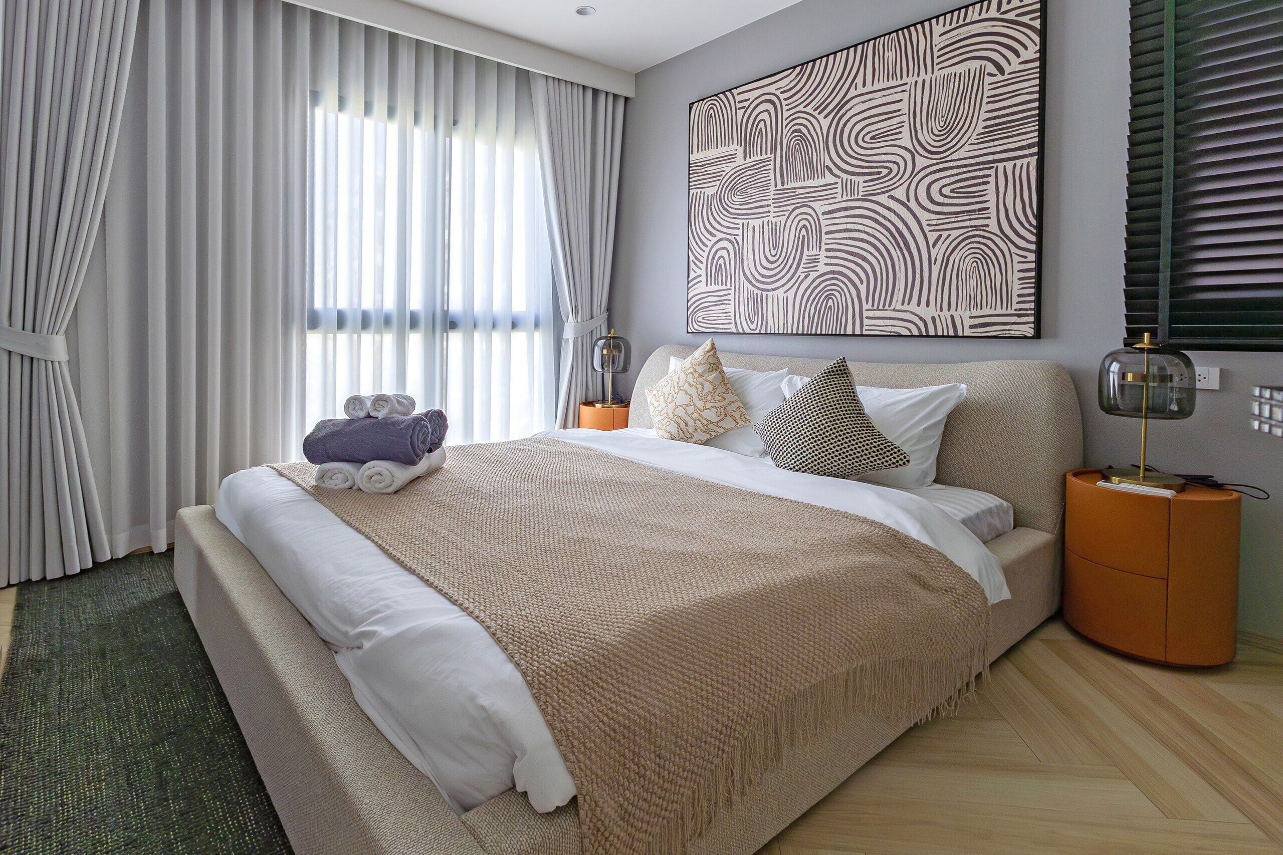 Un dormitorio moderno con una cama grande, un adorno en la pared y una mesita de noche con una lámpara.