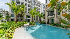 A swimming pool surrounded by lush greenery and modern buildings. - The Title Legendary Designer 2BR near Bang Tao Beach (Tambon Choeng Thale)