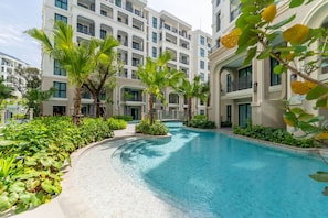 A swimming pool surrounded by lush greenery and modern buildings. - The Title Legendary Designer 2BR near Bang Tao Beach (Tambon Choeng Thale)