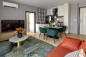 A modern living room with a flat-screen TV, a coffee table with a vase, a green sofa, and a patterned rug. - The Title Legendary Designer 2BR near Bang Tao Beach (Choeng Thale)