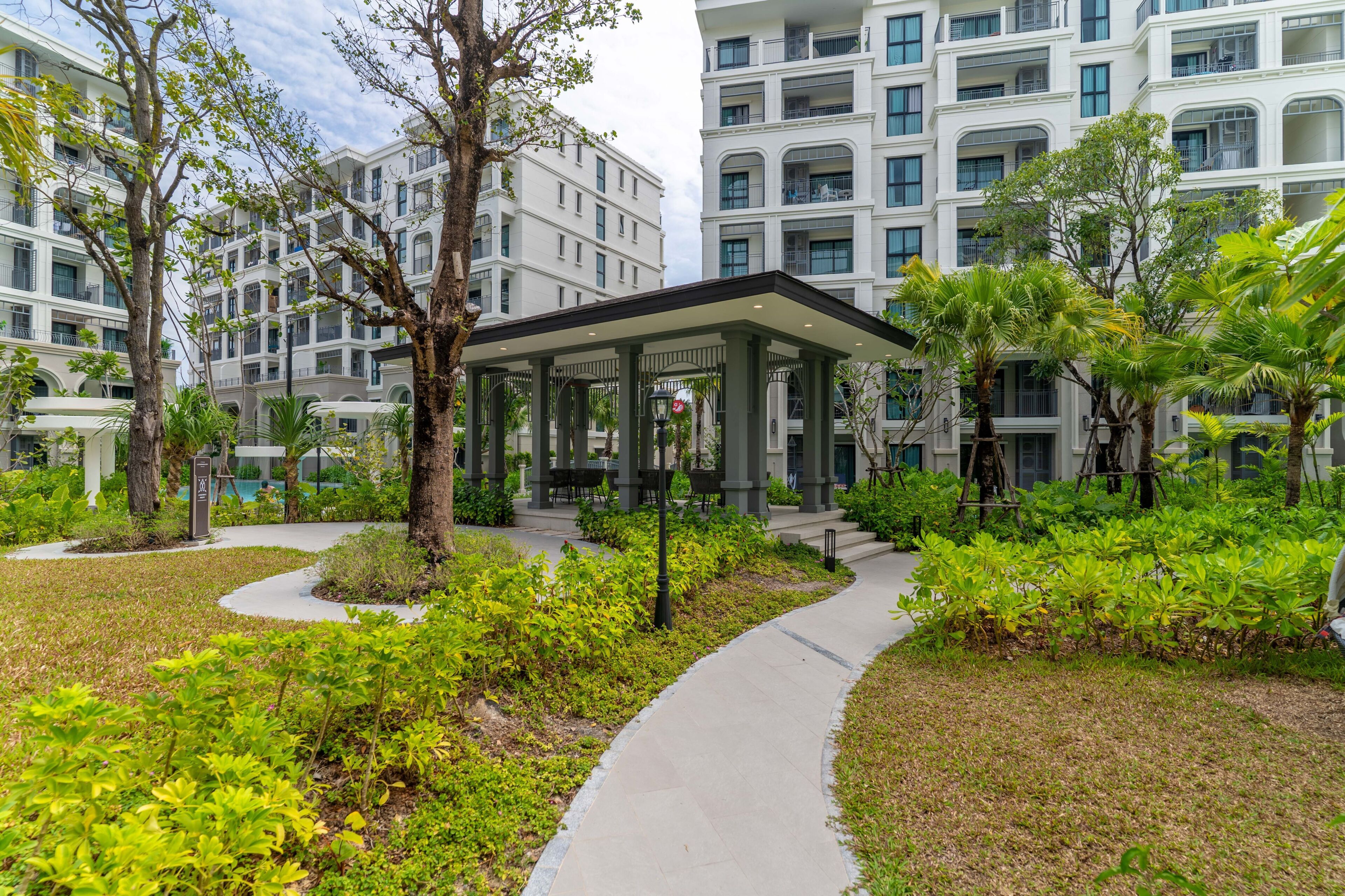 Um edifício moderno com várias varandas, rodeado por vegetação exuberante e um caminho pavimentado.