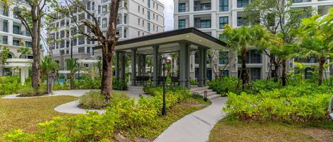 A modern building with multiple balconies, surrounded by lush greenery and a paved walkway.