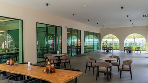 A spacious indoor area with multiple seating arrangements, including tables and chairs, and large windows offering views of greenery outside. - The Title Legendary Designer 2BR near Bang Tao Beach (Tambon Choeng Thale)