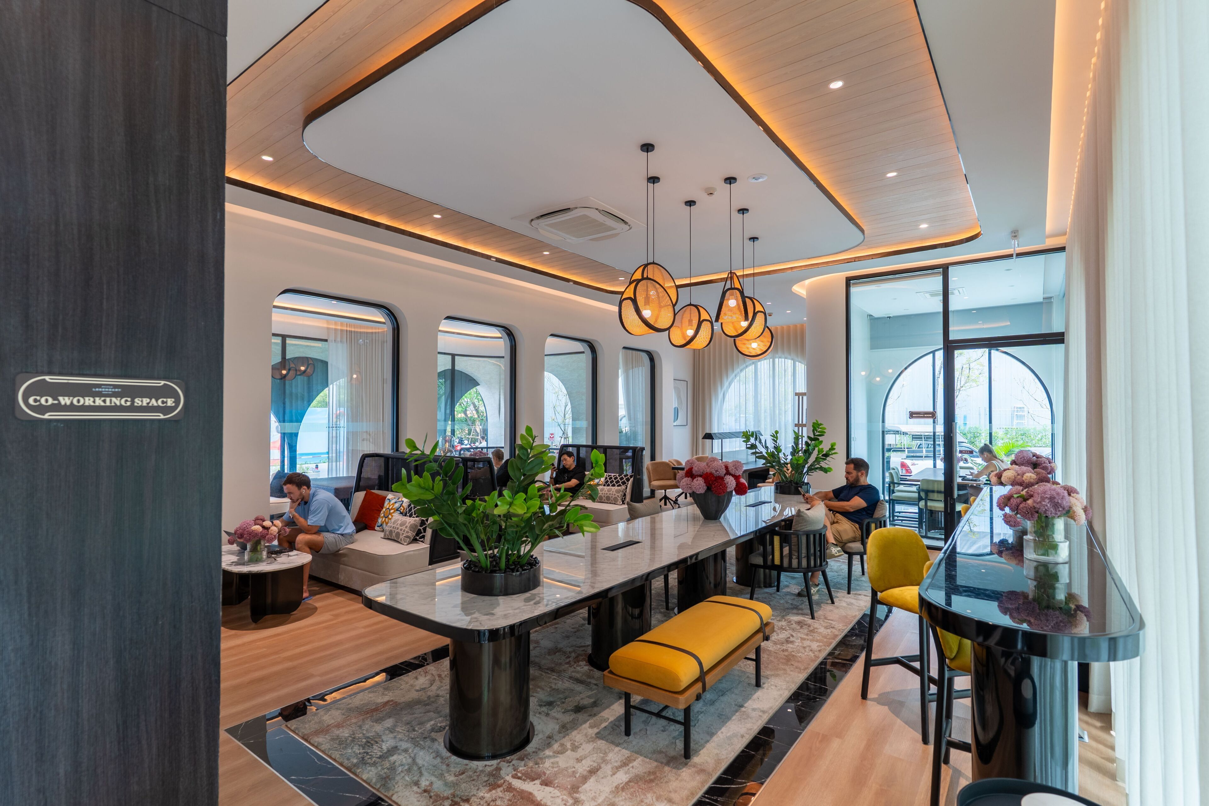 A modern co-working space with a long communal table, individual seating, and large windows.