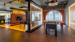 A modern indoor space with a foosball table, arcade gaming area, and a large window providing natural light. - The Title Legendary Designer 2BR near Bang Tao Beach (Tambon Choeng Thale)