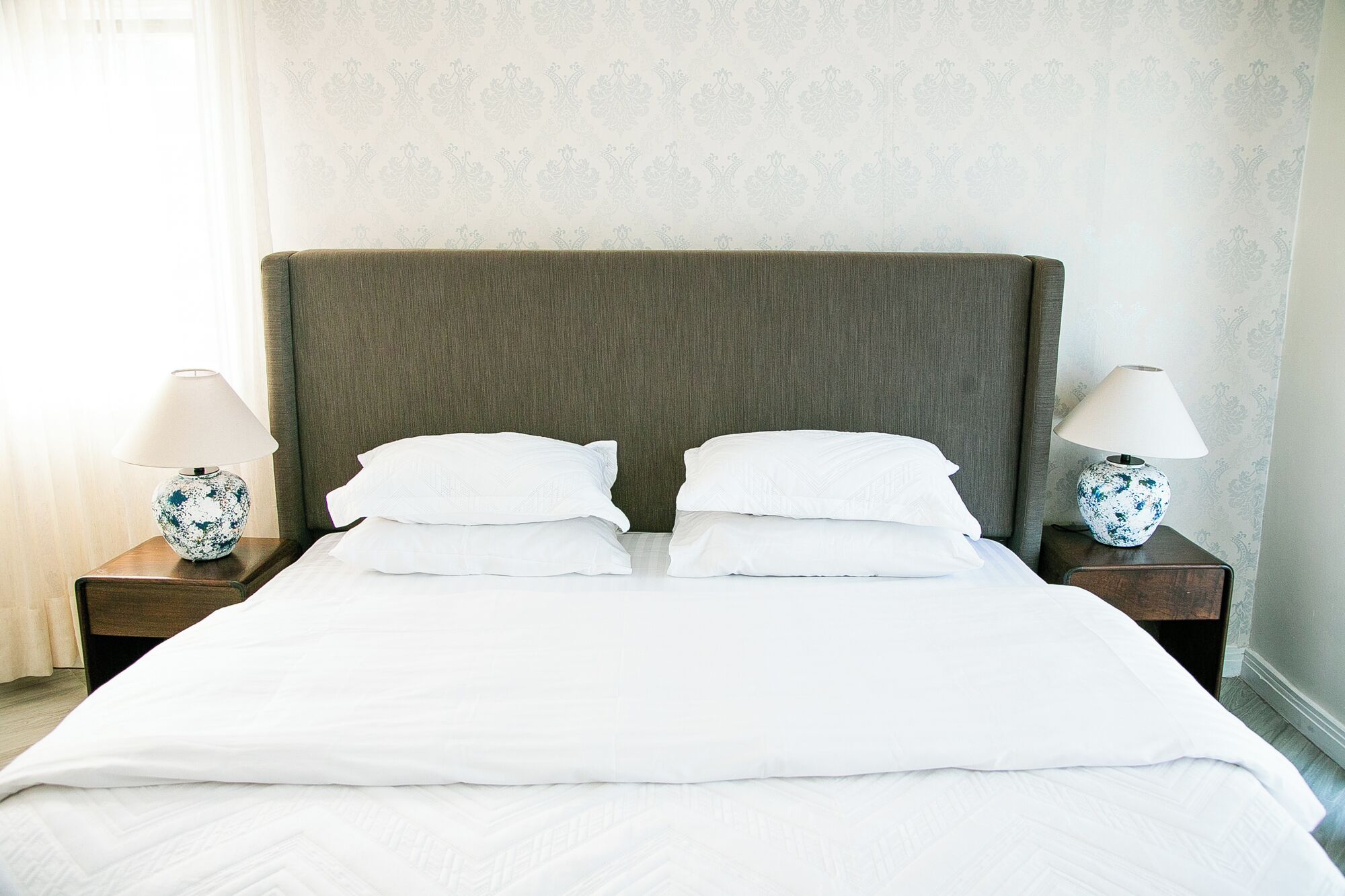 A neatly made bed with white linens, two bedside tables with lamps, and a patterned wallpaper background.