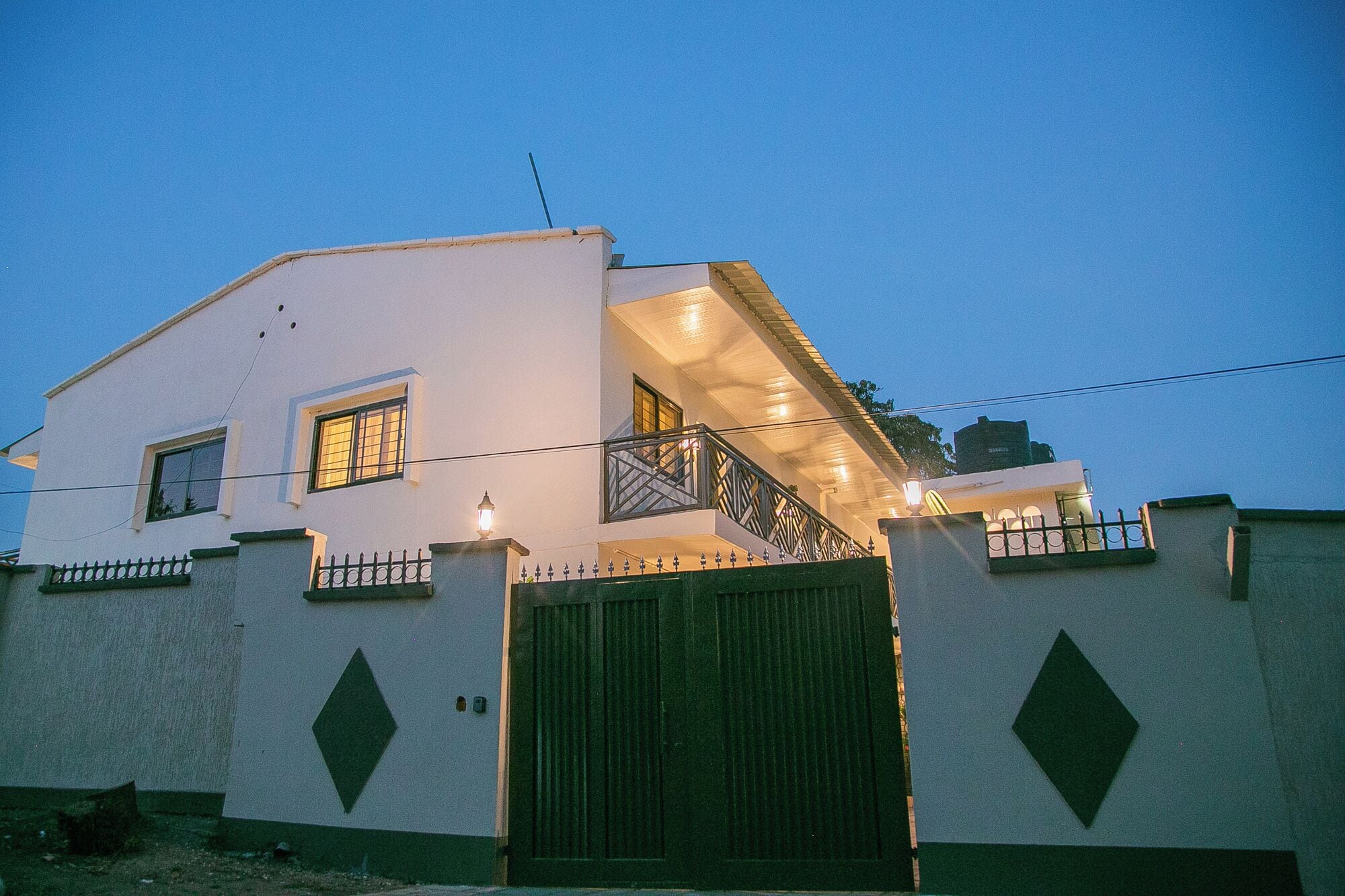 A two-story house with a gated entrance, a balcony with a railing, and a staircase leading to the upper floor.