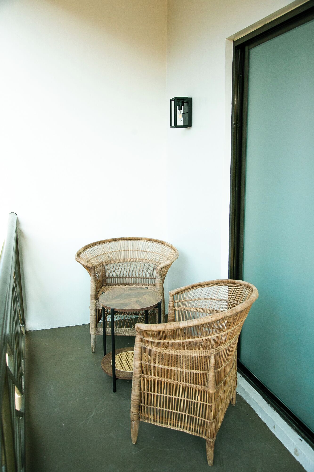 A balcony with wicker furniture, a small table, and a wall-mounted light fixture.