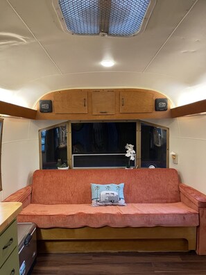 A cozy interior with a sofa, wooden cabinets, and a window. - Vintage Shasta, Glamping for two near Savannah, Hinesville, and Beaches (Midway)