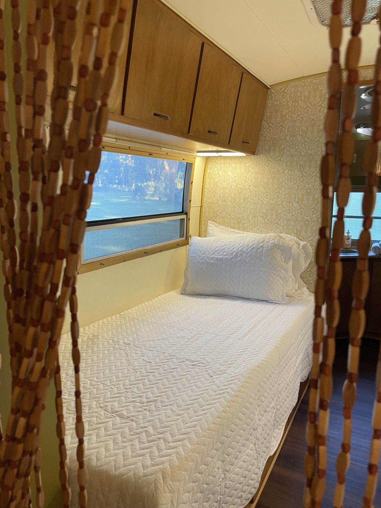 Una cama con colchón acolchado, una ventana con vistas a árboles y armarios de madera.