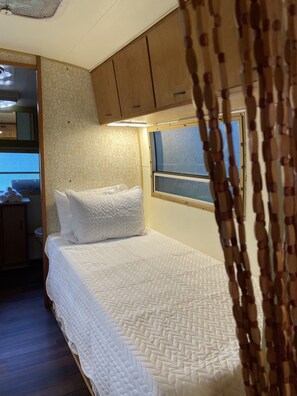 A bedroom with a bed, a window, and wooden cabinets. - Vintage Shasta, Glamping for two near Savannah, Hinesville, and Beaches (Midway)
