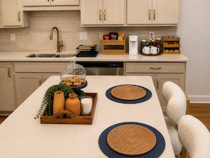 A kitchen with a central island, a coffee maker, and various kitchen items on the counter. - The Willow -  3BR, 3BA Executive Townhome • Boutique Luxury Townhome (Charlotte)