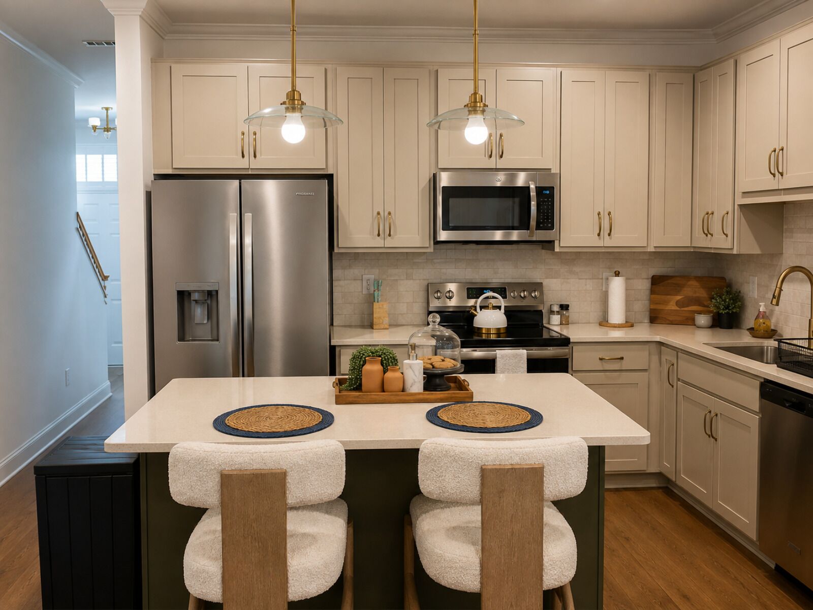 A modern kitchen with stainless steel appliances, a central island with stools, and pendant lighting.