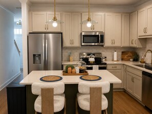 A modern kitchen with stainless steel appliances, a central island with stools, and pendant lighting. - The Willow -  3BR, 3BA Executive Townhome • Boutique Luxury Townhome (Charlotte)