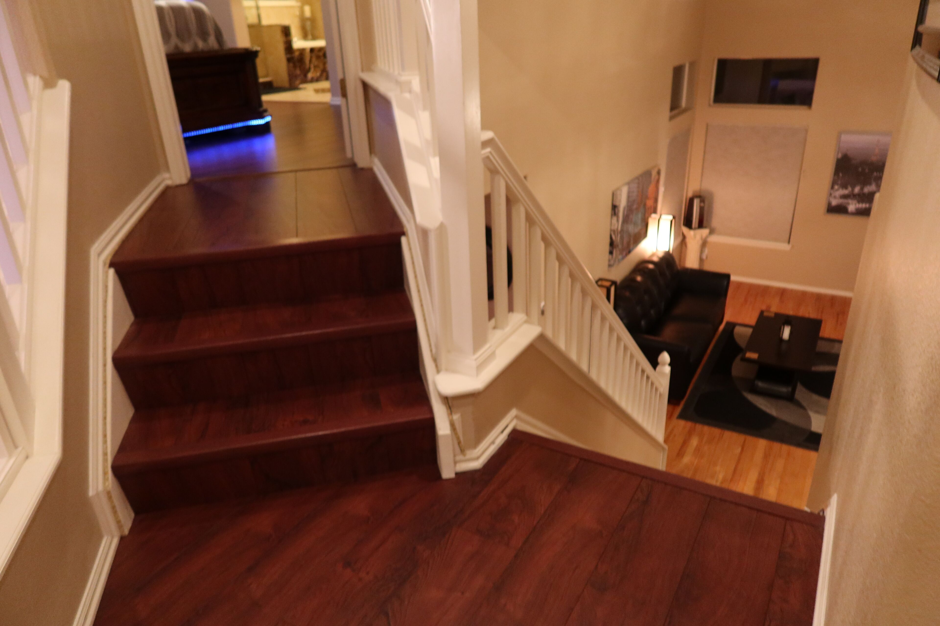 A staircase leading to a living area with a dark wood floor, white railings, and a black leather sofa.