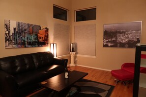 A living room with a black leather sofa, a red chair, a coffee table, a lamp, and two paintings on the walls. - Updated Modern 3-Bedroom Home with Private Hot Tub (Littleton)