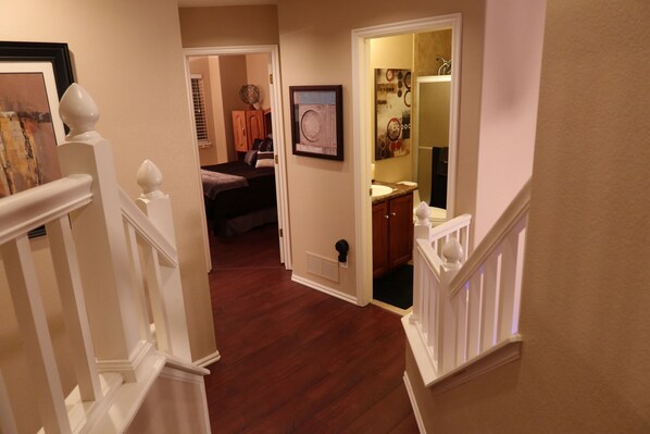 A hallway with a wooden floor leading to a bedroom with a bed and a closet. There is a door leading to a bathroom with a sink and mirror. - Updated Modern 3-Bedroom Home with Private Hot Tub (Littleton)