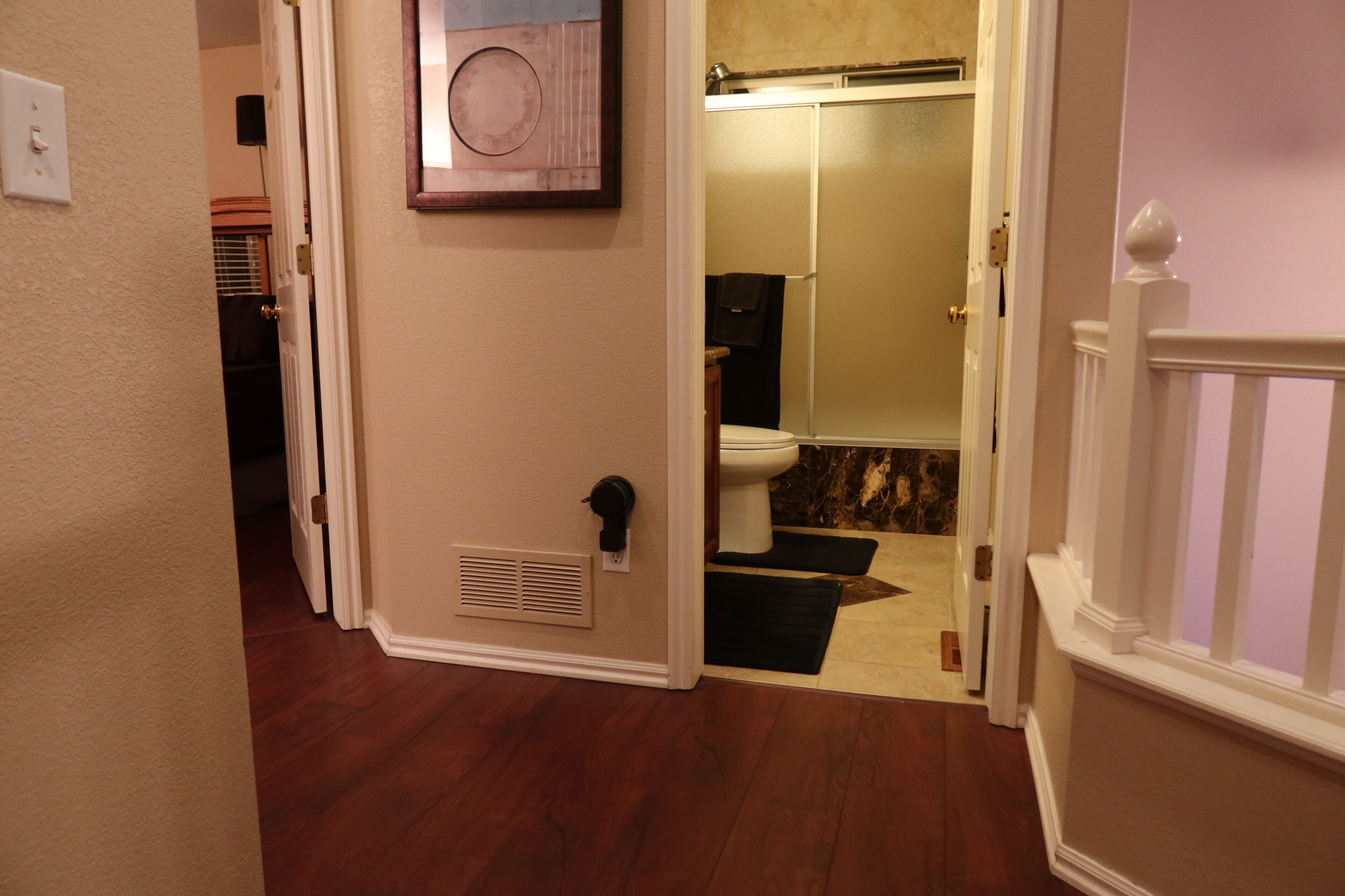 A hallway leading to a bathroom with a toilet, a shower, and a vent on the wall.