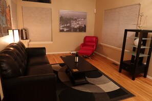 Ein Wohnzimmer mit einer schwarzen Ledersofa, einem roten Sessel, einem schwarzen Couchtisch und einem Stadtbild an der Wand.