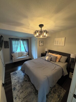 A bedroom with a bed, a window with curtains, a chandelier, and artwork on the walls. - Private cabin retreat with everything you need! (Independence)