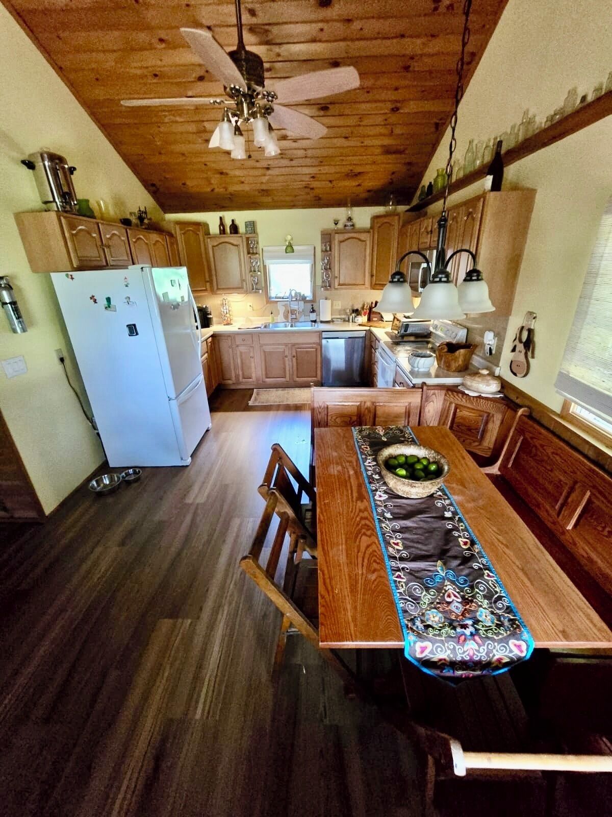 Eine Küche mit Holzschränken, einem weißen Kühlschrank, einem Esstisch mit dekorativer Tischdecke und einem Deckenventilator.