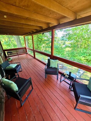 A covered outdoor deck with wooden flooring, metal railings, and seating areas.