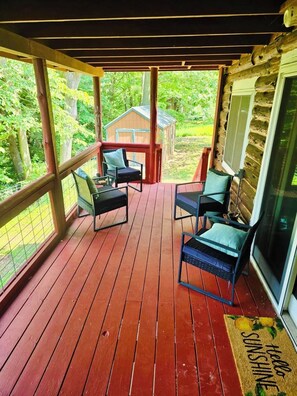 A covered porch with wooden flooring, two chairs, a small table, and a view of a garden and a shed. - Riverfront log cabin with 200 feet private water front and beautiful views !  (Pulaski)