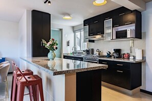 Eine moderne Küche mit dunklen Schränken, einer Granit Arbeitsplatte, Edelstahlgeräten und einem Blumenstrauß auf der Kücheninsel.