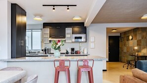 A modern kitchen with dark cabinets, a central island with stools, and a dining area with a table and chairs. - Designer Apt in Roma Norte, Parking & Workspace (Mexico City)