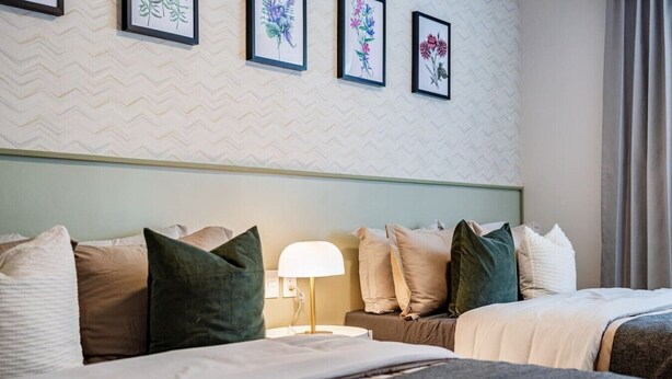 A hotel room with two beds, a nightstand with a lamp, and a wall with framed floral artwork. - Designer Apt in Roma Norte, Parking & Workspace (Mexico City)