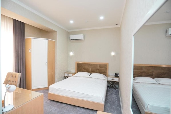 A hotel room with a single bed, bedside tables, a desk, and an air conditioning unit. - Reikartz Amirun (Tashkent)