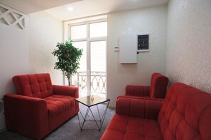 A room with two red sofas, a small table, a potted plant, and a window with a view. - Reikartz Amirun (Tashkent)