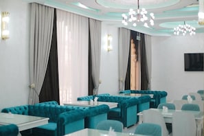 A modern dining area with teal upholstered sofas, glass tables, and a chandelier. - Reikartz Amirun (Tashkent)