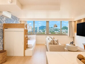 Ein modernes Hotelzimmer mit Bett, Sofa, Fernseher und Blick auf die Stadtlandschaft.